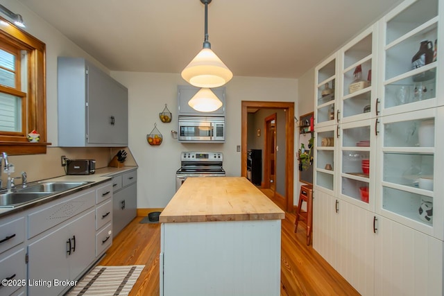 kitchen with butcher block countertops, sink, hanging light fixtures, stainless steel appliances, and a center island