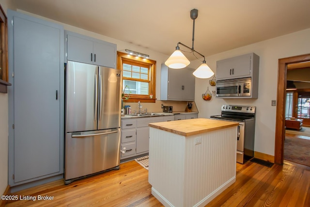 kitchen with stainless steel appliances, wooden counters, a center island, pendant lighting, and a healthy amount of sunlight