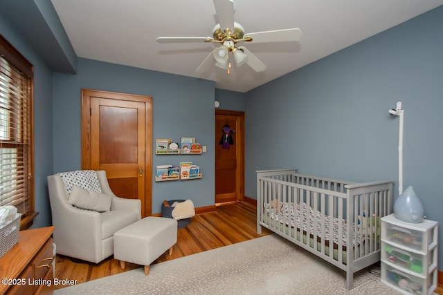 bedroom with a nursery area, ceiling fan, and wood-type flooring