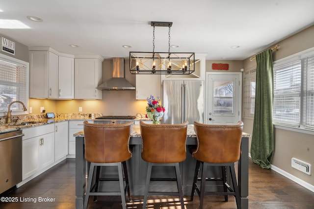 kitchen featuring sink, appliances with stainless steel finishes, hanging light fixtures, white cabinets, and wall chimney exhaust hood