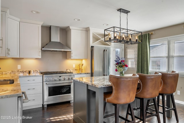 kitchen with white cabinetry, premium appliances, light stone countertops, decorative light fixtures, and wall chimney exhaust hood