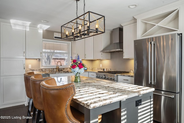 kitchen featuring sink, hanging light fixtures, light stone counters, stainless steel appliances, and wall chimney exhaust hood