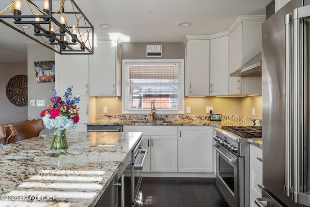 kitchen featuring sink, wall chimney range hood, white cabinetry, stainless steel appliances, and decorative light fixtures