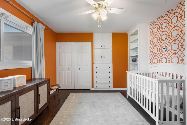 bedroom with dark hardwood / wood-style floors, a crib, a closet, and ceiling fan