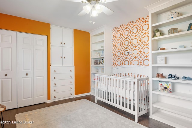 bedroom with a crib, dark hardwood / wood-style floors, ceiling fan, and a closet