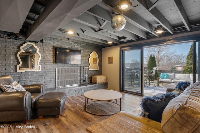 living room featuring wood-type flooring, brick wall, a fireplace, and beam ceiling