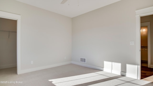 unfurnished bedroom with ceiling fan, a walk in closet, light carpet, and a closet