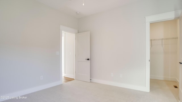 unfurnished bedroom with a walk in closet, light colored carpet, and a closet