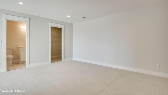 unfurnished bedroom with a walk in closet, light carpet, connected bathroom, and a closet