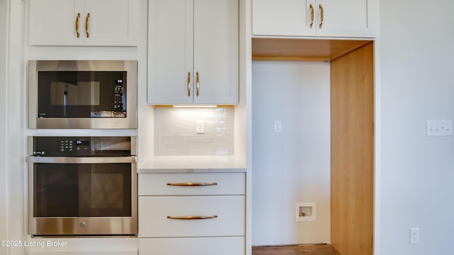 kitchen with built in microwave, tasteful backsplash, white cabinets, stainless steel oven, and light stone countertops