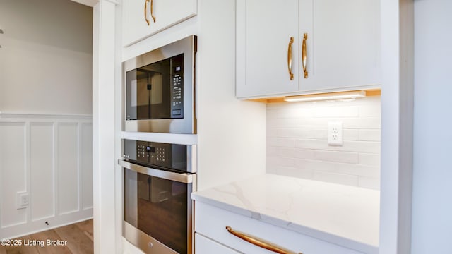 kitchen with white cabinetry, light stone counters, tasteful backsplash, and appliances with stainless steel finishes