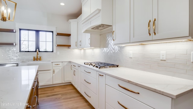 kitchen with sink, white cabinetry, light stone counters, decorative light fixtures, and stainless steel gas stovetop