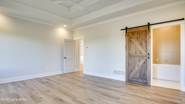 empty room with ceiling fan, a tray ceiling, crown molding, a barn door, and light hardwood / wood-style flooring