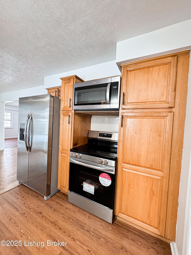 kitchen featuring appliances with stainless steel finishes, light hardwood / wood-style floors, and a textured ceiling