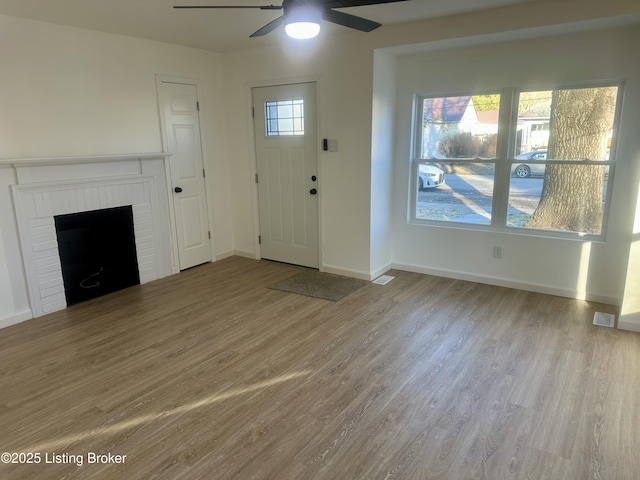 foyer entrance featuring ceiling fan, a wealth of natural light, a fireplace, and light hardwood / wood-style flooring