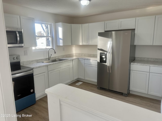 kitchen with appliances with stainless steel finishes, sink, white cabinets, and dark hardwood / wood-style flooring