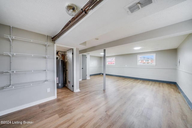 basement with light hardwood / wood-style floors, water heater, and a textured ceiling