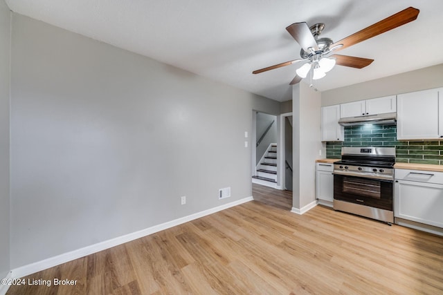 kitchen featuring stainless steel stove, light hardwood / wood-style flooring, ceiling fan, white cabinetry, and decorative backsplash