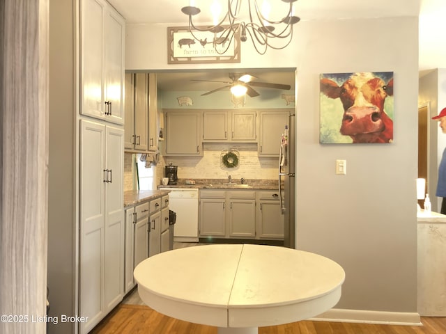 kitchen with sink, stainless steel fridge, white dishwasher, pendant lighting, and light stone countertops