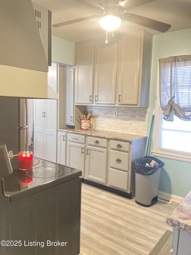 kitchen featuring stainless steel refrigerator, white cabinets, decorative backsplash, range, and light wood-type flooring