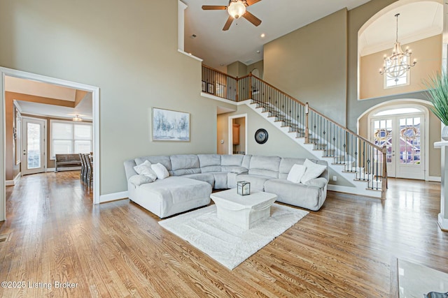 living area with stairs, light wood finished floors, ceiling fan with notable chandelier, and baseboards