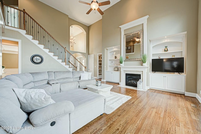 living room with arched walkways, a towering ceiling, baseboards, built in features, and light wood-type flooring