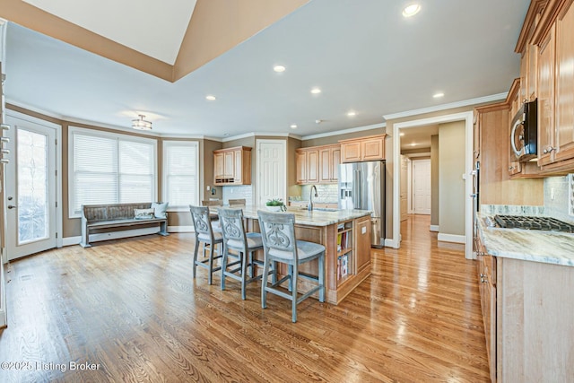 kitchen featuring light stone counters, a kitchen island with sink, appliances with stainless steel finishes, decorative backsplash, and a kitchen bar