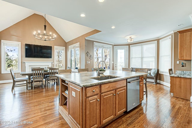 kitchen featuring an island with sink, light stone counters, brown cabinets, and a sink