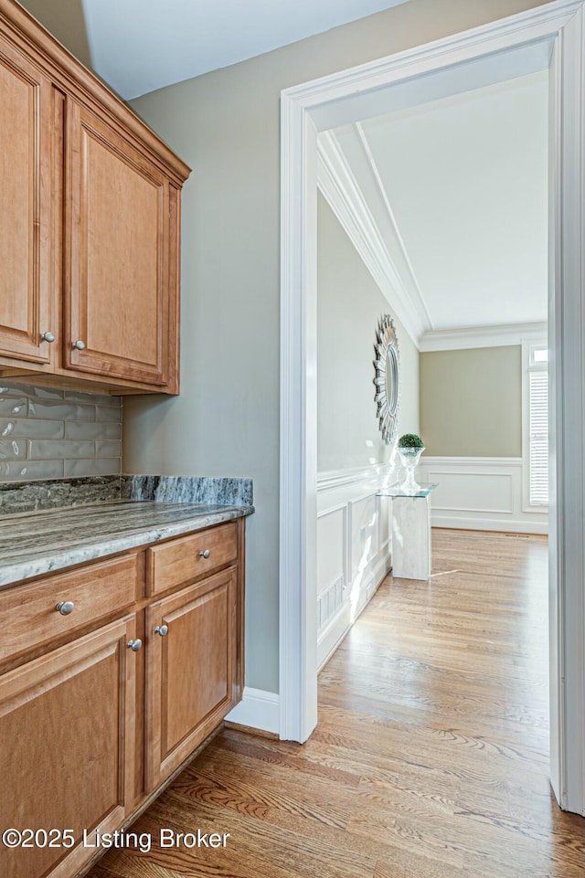 bar featuring visible vents, decorative backsplash, a wainscoted wall, crown molding, and light wood-style floors