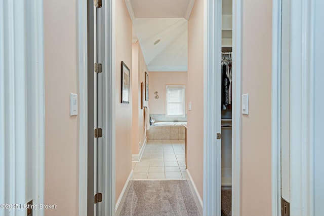 corridor featuring light colored carpet, vaulted ceiling, baseboards, and light tile patterned floors