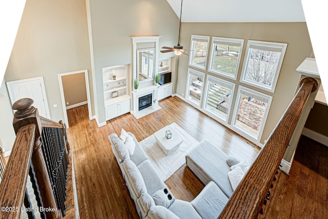 living room with a fireplace with flush hearth, a ceiling fan, wood finished floors, high vaulted ceiling, and baseboards