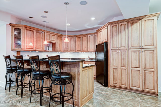 kitchen featuring a breakfast bar area, freestanding refrigerator, a center island, glass insert cabinets, and pendant lighting