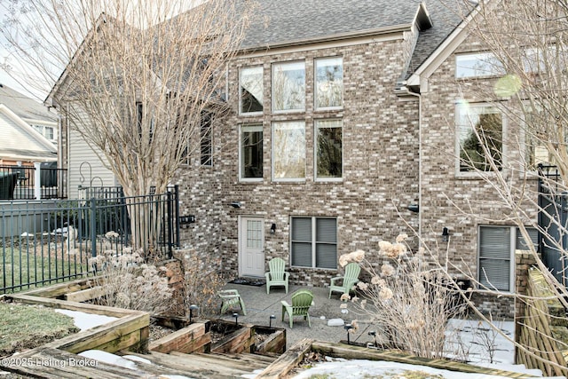 view of front facade featuring a shingled roof, a garden, a patio area, and brick siding