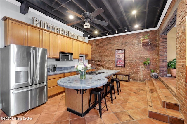 kitchen featuring a kitchen island, tile counters, stainless steel appliances, and brick wall