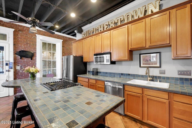 kitchen featuring brick wall, appliances with stainless steel finishes, sink, tile counters, and light tile patterned floors