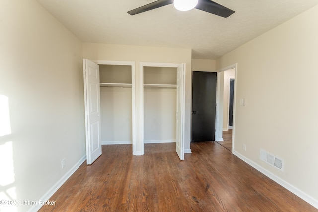 unfurnished bedroom featuring ceiling fan, dark hardwood / wood-style floors, and two closets