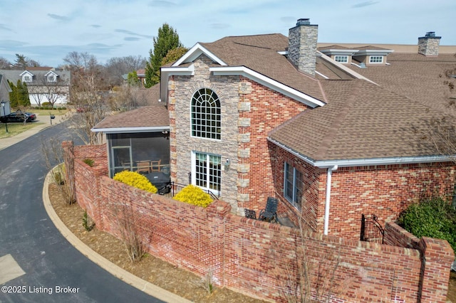 view of home's exterior with a sunroom, a shingled roof, a chimney, and brick siding