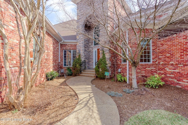 view of exterior entry featuring roof with shingles and brick siding