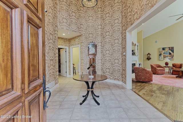 entryway with wallpapered walls, baseboards, a fireplace, and high vaulted ceiling