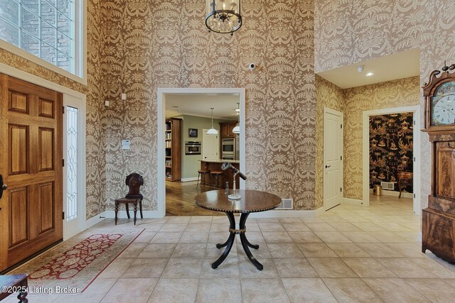 entryway featuring a towering ceiling, wallpapered walls, visible vents, and baseboards