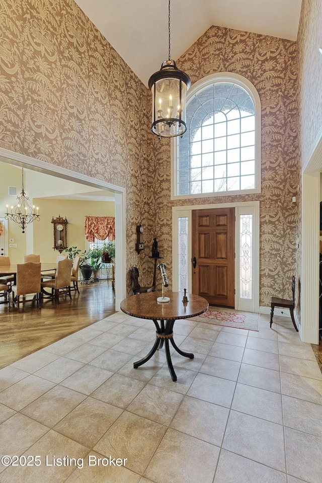 entrance foyer featuring wallpapered walls, tile patterned flooring, high vaulted ceiling, and an inviting chandelier