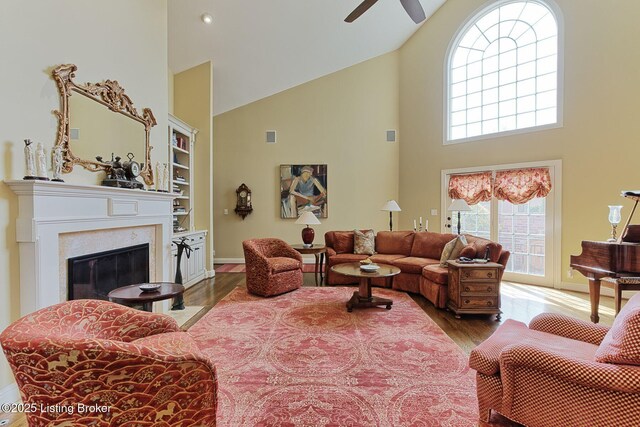 living area with ceiling fan, built in shelves, a premium fireplace, wood finished floors, and a towering ceiling