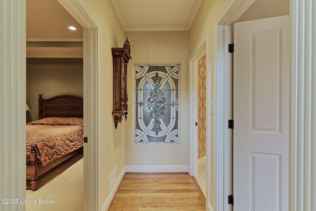 corridor with light wood-type flooring, baseboards, visible vents, and ornamental molding