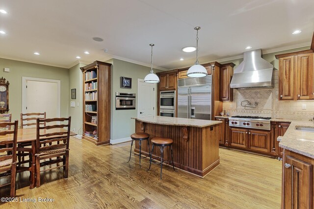 kitchen featuring light wood finished floors, decorative backsplash, stainless steel appliances, wall chimney range hood, and a sink