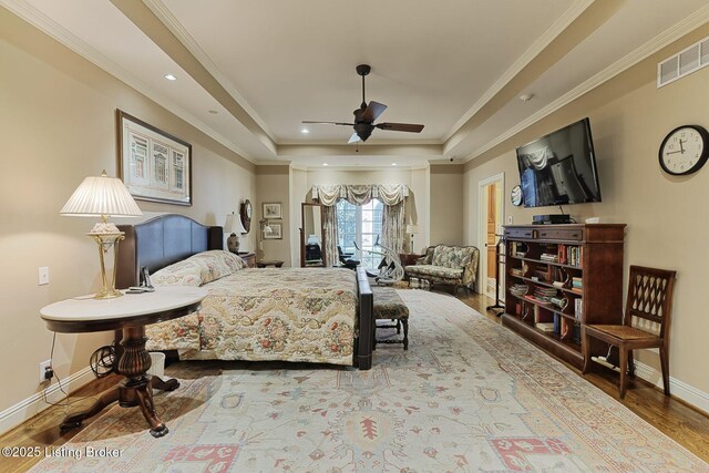 bedroom featuring wood finished floors, visible vents, baseboards, ornamental molding, and a tray ceiling