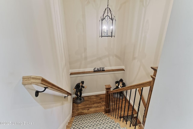 stairway with an inviting chandelier, baseboards, and wood finished floors