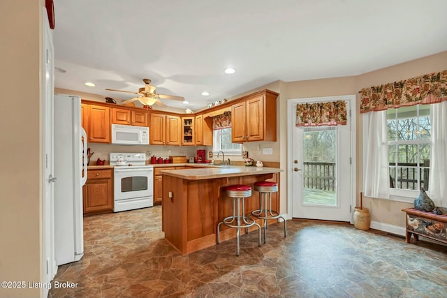 kitchen with sink, white appliances, a breakfast bar, a wealth of natural light, and kitchen peninsula