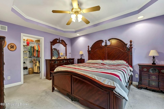 carpeted bedroom with a closet, a walk in closet, crown molding, and a tray ceiling