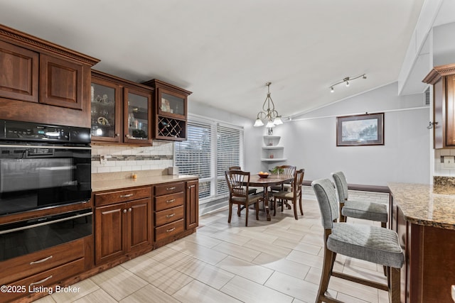 kitchen featuring decorative light fixtures, vaulted ceiling, black oven, light stone countertops, and decorative backsplash