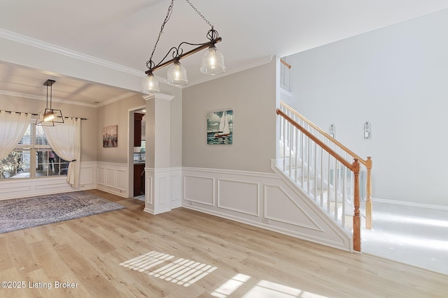 unfurnished dining area with crown molding, decorative columns, and light wood-type flooring